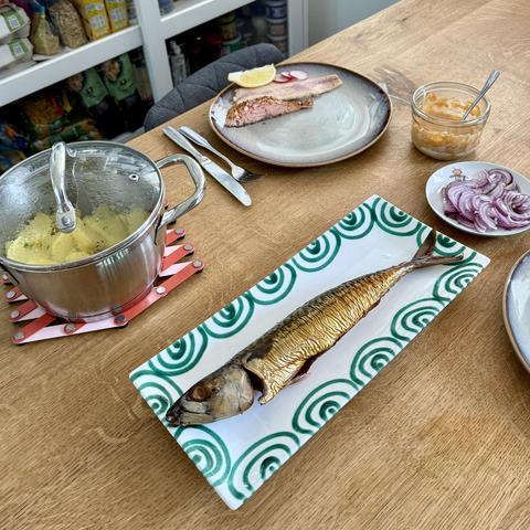 A photo showing parts of the table with a half filled plate, the potatoes in their saucepan, the mayo dip, and in the centre a dish with the whole smoked mackerel.