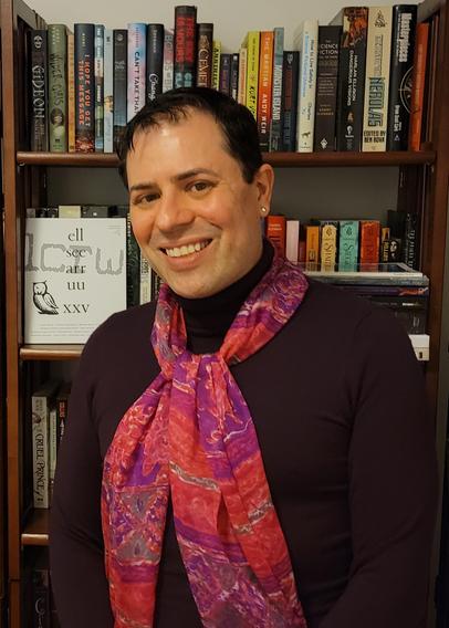 Waist-up color photo of writer Ben Francisco, a Latinx person with dark hair worn short, dark eyes, and perfectly arched eyebrows. They wear a dark brown turtleneck, a long scarf patterned in swirls of bright, warm colors, and gold stud earrings. They stand in front of a bookcase full of speculative fiction titles and smile warmly into the camera.