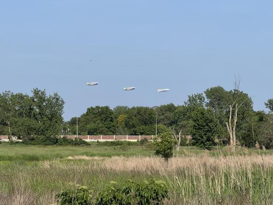 Three Goodyear blimps flying over downtown Akron. Photo taken from out in the country while on a bike ride. The blimps are in a line at roughly the same altitude.