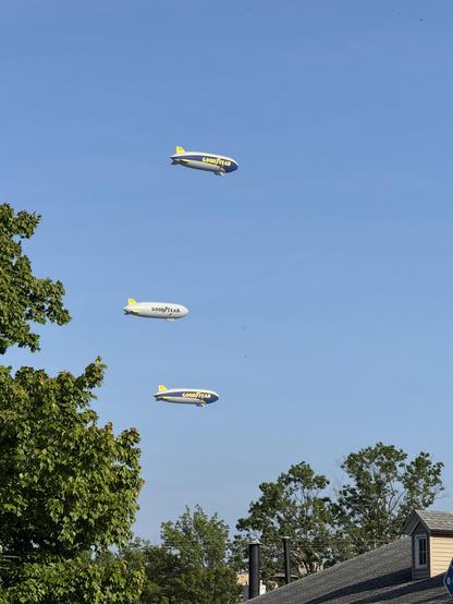 Three Goodyear blimps flying over downtown Akron. Photo taken from in Highland Square while on a bike ride. The blimps are stacked at different altitudes.