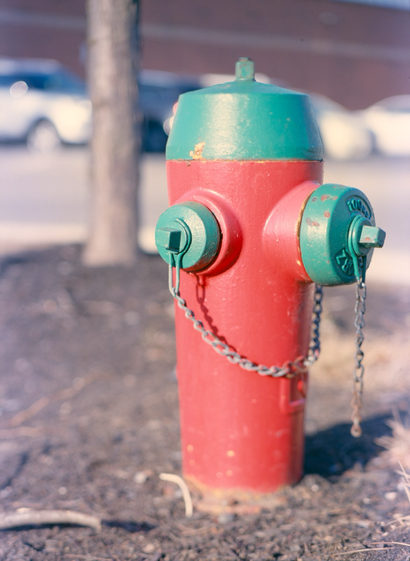 A bright red fire hydrant with green crown and connections.