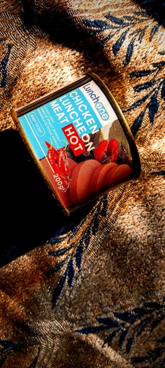 The photograph composed in total darkness features a can of "Lunchone Chicken Lunch Meat Hot" placed on a textured fabric with a blue and gold pattern. The can is positioned diagonally, with the label facing the viewer. The label is predominantly blue with white and red text. The text reads "Lunchone Chicken Lunch Meat Hot" with "Hot" in a red box, indicating the spiciness level. Below the main text, there is a depiction of red chili peppers and the weight "200g" is visible. The can is labeled as "Ready to Eat." The background fabric has a woven texture with a mix of blue and gold colors, creating a warm and inviting appearance.

 Ovis2-8B

🌱 Energy used: 0.179 Wh