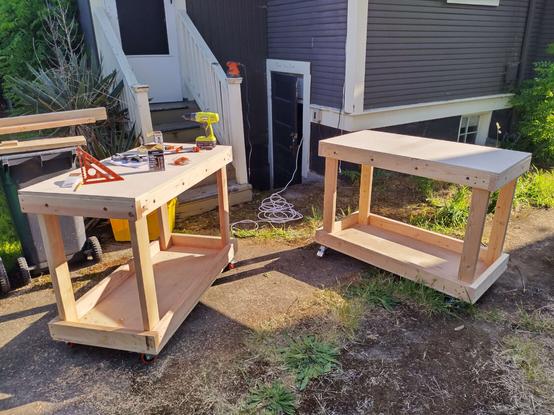 Two barebones wooden carts and some assorted tools sitting outside in the evening sun.