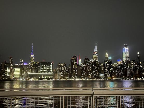 Photo looking across the East River at the Manhattan Midtown skyline, and OMG, there's a very tall but big-ass blocky building toward the right that is lit up like everybody, everybody, is working late.
