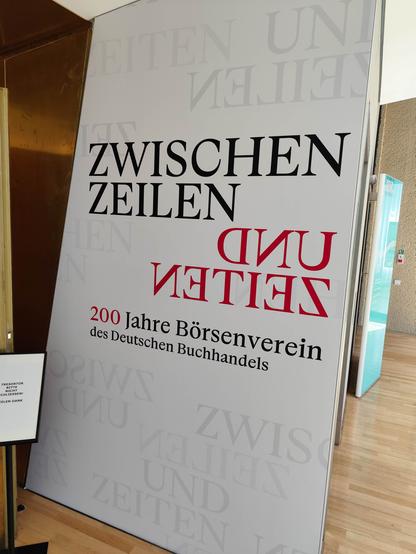 Großes Hinweisschild zur Ausstellung "Zwischen Zeilen und Zeiten" (identisch mit dem Cover des zugehörigen Buchs (Wallstein); DNB Leipzig.
