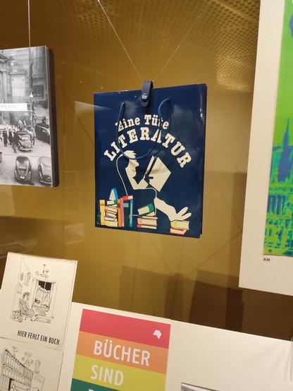 Objekt in der Ausstellung "Zwischen Zeilen und Zeiten": eine blaue Tüte mit Aufschrift "Eine Tüte Literatur", sowie einem lesenden Mann mit zufriedenem Gesichtsausdruck in einem Ohrensessel; DNB Leipzig.