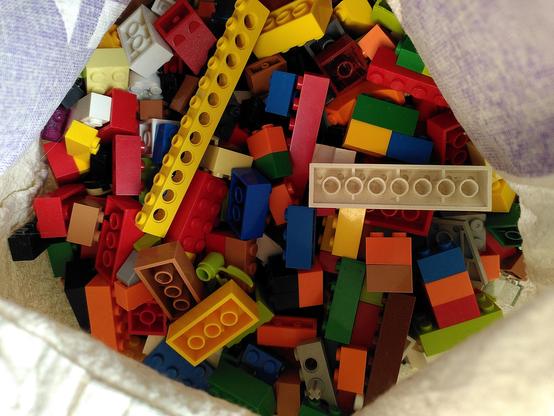 Blick in einen Beutel mit bunten Legosteinen, die kreuz und quer durcheinander liegen.