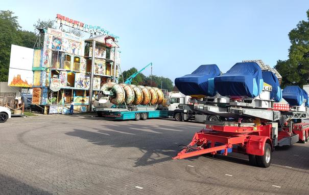 Karussell Kabinen und Karussellteile auf LKW Anhängern verpackt. Ein Kran hebt gerade ein Teil hoch. Ein sogenannter "Lachsalon" ist schon fast fertig aufgebaut.