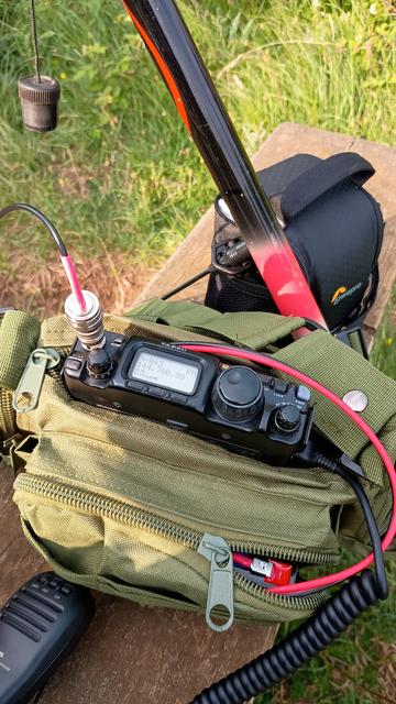 FT-817 in a green canvas bag. There is a cable attached to the BNC antenna socket on the front of the radio. The frequency 144.700MHz is displayed.