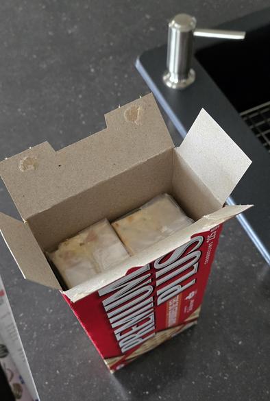 A box of salted cookies standing on a counter top, on one of it's ends, just opened. You can see over 2 inches of empty space over the unopened cookie enveloppes.