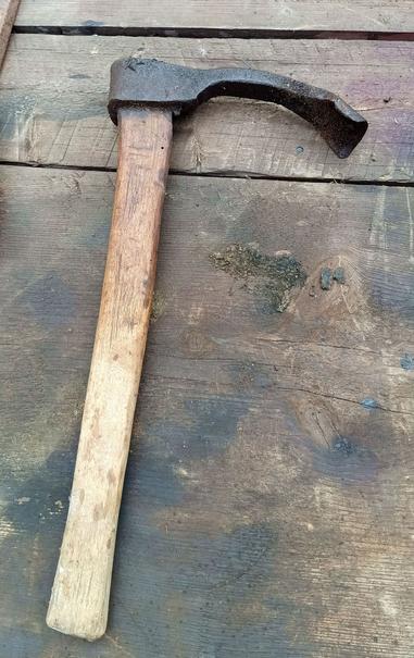 A medium size adze on a table. If you're unfamiliar, an adze is like an axe, only it chops at a 90 degree angle. This one has a curved blade, perfect for hollowing out things or building log houses. The steel head and top of the wooden handle are well preserved due to being accidentally coverd in grease from a leaky grease gun next to it.
