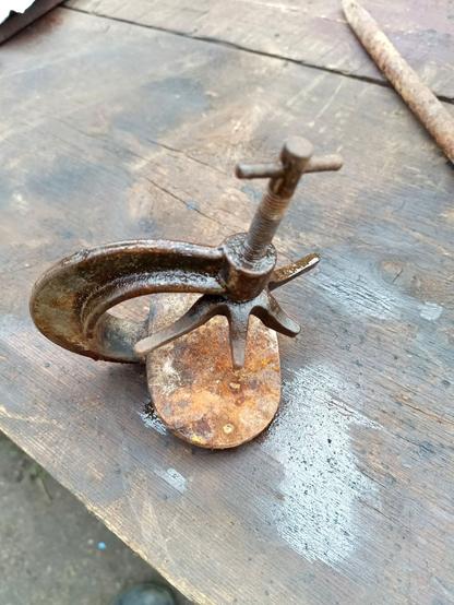 A small press. It consists of a reinforced arch with a wide flat plate on the bottom. The moving part consists of a threaded rod with a short handle and a six pronged clamp at the bottom where two opposing fingers are longer than the rest and the bottom is concave. It would probably make a good walnut cracker.