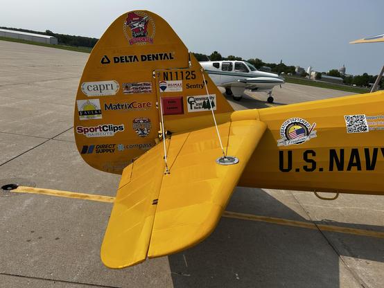 Aircraft tail of a Stearman, in classic yellow paint. Every available surface of the vertical stabilizer is covered in stickers of the sponsors supporting this aircraft