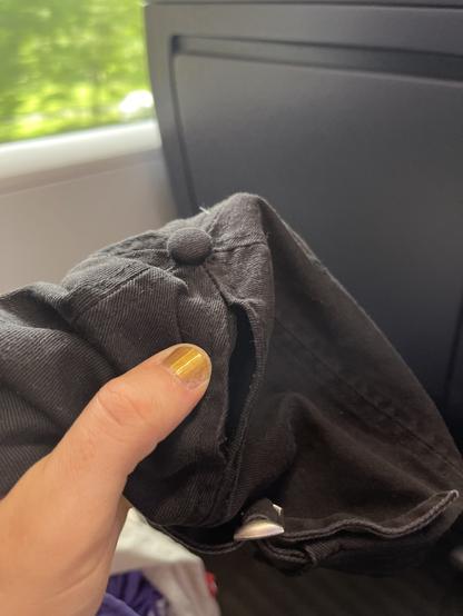 Rückseite einer Schirmmütze. Die mittleren 60% der mittleren Rückennaht sind aufgetrennt für die besagte Öffnung. Im Hintergrund sieht man Fenster und Sitz des ICEs in dem ich fahre.