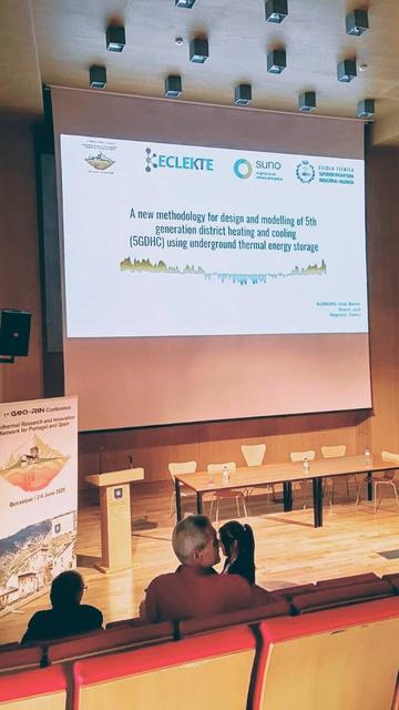 Foto de la sala de conferencies des del públic amb la portada de la presentació projectada a la pantalla on es veuen tres persones.