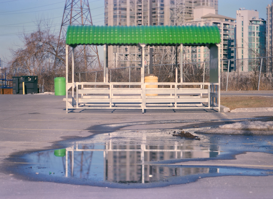 A aluminum structure with a bright green roof, a shelter to return your shopping carts, stands empty in an empty parking lot.