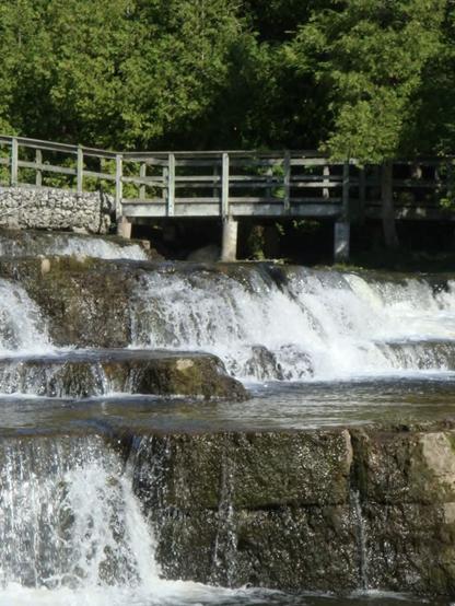 A wooden walkway overlooks mini layered waterfalls and rocks of Sauble Falls