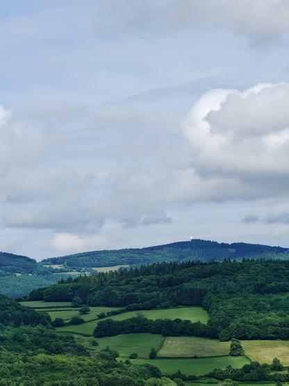Vue de vertes collines morvandelles, avec quelques champs et des forêts, sous un ciel très nuageux. On distingue au loin le radome clair d'un radar de contrôle du traffic aérien civil.