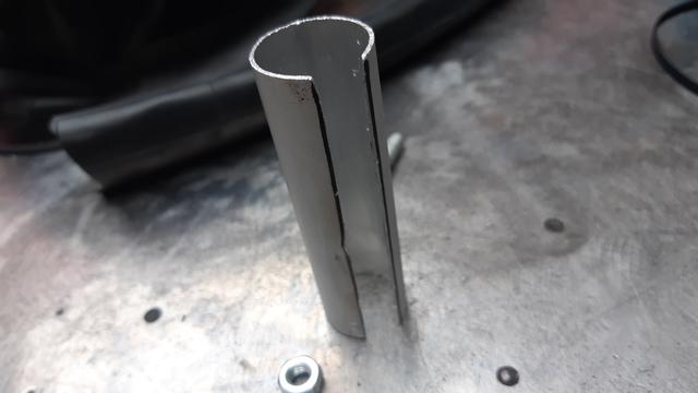 Tube de balai en aluminium taillé pour servir de socle à un mat porte comm, sur une table d'atelier en métal
