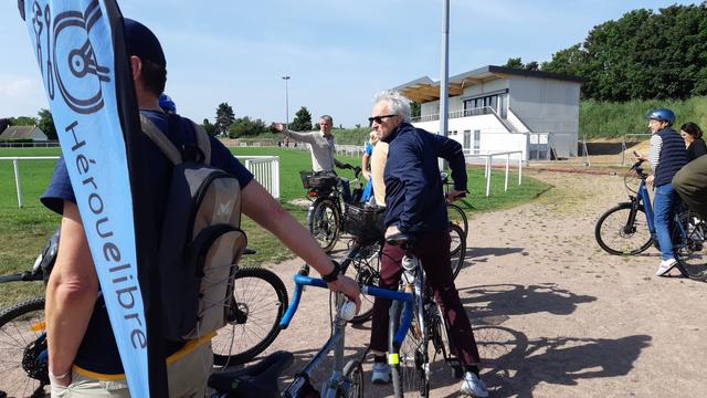 Membres de l'équipe municipale d'Hérouville Saint-Clair dont le maire M Thomas et bénévole d'Hérouelibre tenant son vélo porte-drapeau, près d'un terrain de rugby.