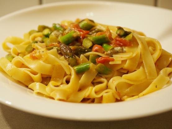 Eine Portion Pasta mit Bandnudeln mit einer Sauce aus grünem Spargel, Gorgonzola und Tomaten auf einem weißen Teller