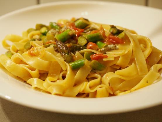 Eine Portion Pasta mit Bandnudeln mit einer Sauce aus grünem Spargel, Gorgonzola und Tomaten auf einem weißen Teller