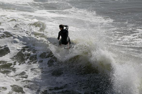 A surfer in a black wetsuit rides a breaking wave in Santa Cruz, California, surrounded by foamy white water and dynamic surf action.