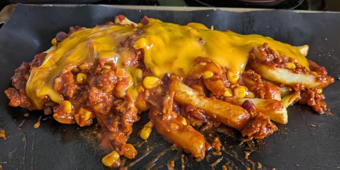 Eine schwarze Unterlage auf der die Pommes liegen. Belegt mit Chili non Carne und geschmolzenem Käse.