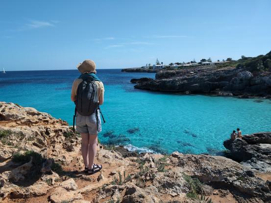 A woman standing near the edge of a cliff with clear blue water below