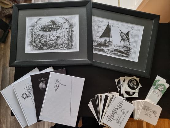 Zu sehen sind 2 gerahmte Bilder, 4 Bücher und jede Menge Give-Aways wie Postkarten, Bierdeckel, Lesezeichen und Sticker