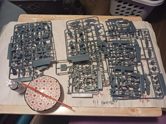 A photograph of Beatrix's crafting table. It's covered entirely in command wolf sprues stacked two high, all in one uniform colour, plus the painting bowl and the tube of lead grey paint that is going to have to coat nearly everything here.