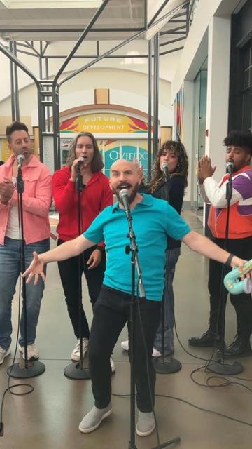 VoicePlay (Geoff Castellucci, Layne Stein, Eli Jacobson, Cesar De La Rosa, and guest Ashley Diane) singing at microphones inside Oviedo Mall in Florida.