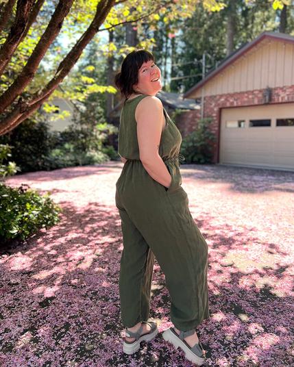 Helen wears a sleeveless green linen Lazo Jumpsuit in her garden.