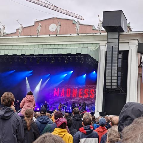 A stage, quite far away, with a band, and the word Madness in strong red on the backdrop.