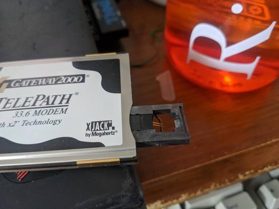 "XJACK" connector on a modem PC Card (PCMCIA card). It's a little piece that pops out of the side of the card when you press in on it, like a nintendo DS cartridge or an SD card. But then there's an RJ connector shaped hole in the part that sticks out, with a wire bar that pushes down to prevent an RJ connector from going all the way through it (you can see through the back of it). There's contacts of spring type metal that are just exposed and totally lose that an RJ connector should make contact with when pushed in from above. This one is for a 33.6 modem.