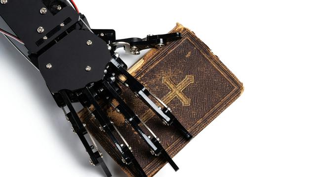 A robot hand holding an old Christian Bible.