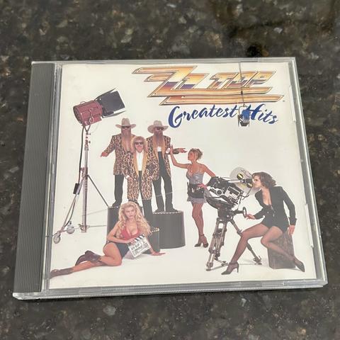 ZZ Top’s Greatest Hits CD, used. The cover features the band in western attire with models, lights, and a camera.