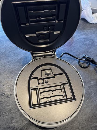The opened waffle iron. It shows the negative of the waffle that will come from it. It is Artoo‘s dome and upper body to his utility arms.