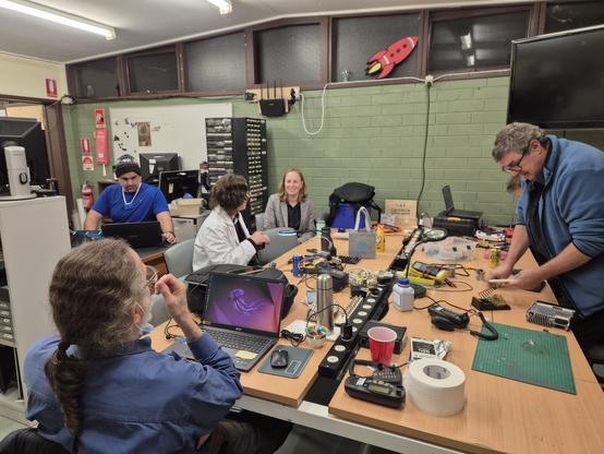Five people sitting around a table at Canberra Makerspace working away at projects and just hanging out