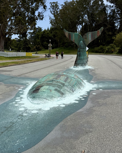 Humpback whale art merging into the road, with back and tail above ground.