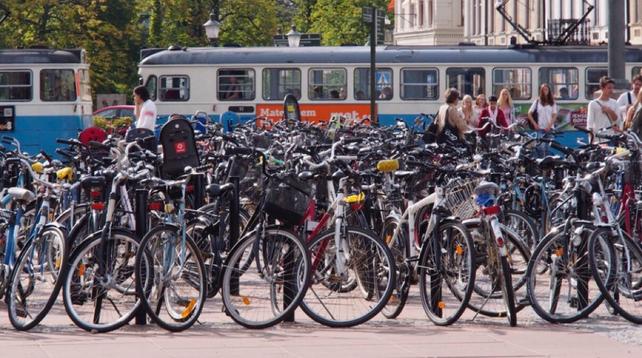 Photo of bikes, parked in a square with a tram going by behind