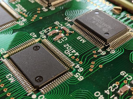 PCB with a square hole routed out of it and a surface mount chip suspended inside of the space by its leads