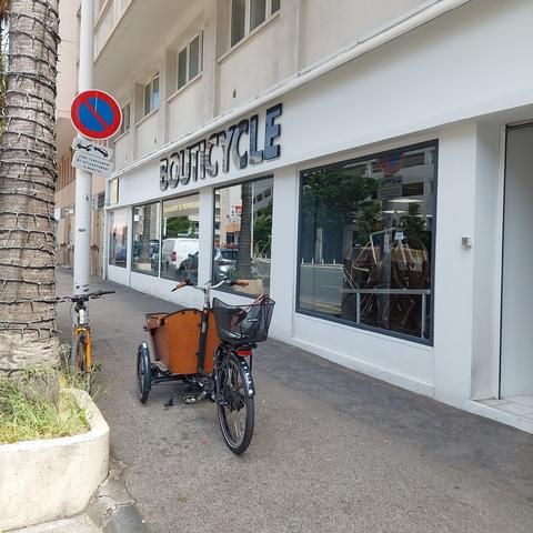 Photo de deux vélos, un VTT et un triporteurs, garés sur le trottoir devant la boutique "bouticycle".