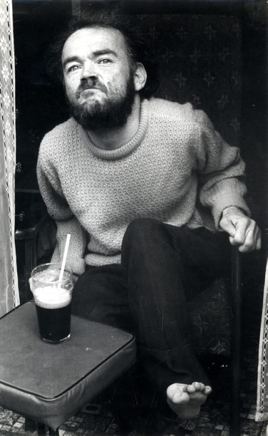 Christy Brown sitting in front of a pint of stout with a straw.