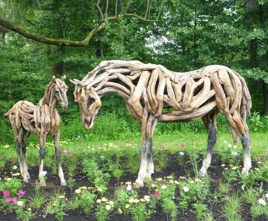 Photo of a horse and foal created with driftwood sited on a flower bed in a garden next to woodlands