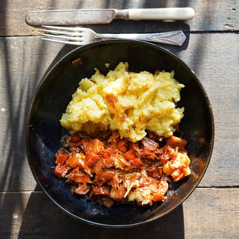 Dunkler Holzuntergrund. Darauf eine schwarze Bowl. Darin: Geschmortes Gemüse der Saison mit Sauerkraut und Kartoffelpüree