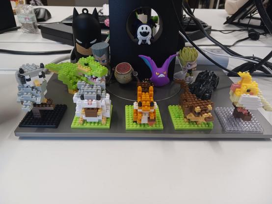 A number of miniature Lego characters. In the front there are an owl, a hamster, a squirrel, a dog, a bird. In the background there's a Lego dinossaur. There are other miniatures not made of Lego: A warrior jar (elden ring), crobat (pokemon), Dio and Polnareff (jojo), batman and a batmobile. All miniatures.