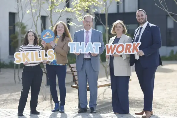 Photograph of four people stood outside holding on to cut out signs that spell out "Skills that work"