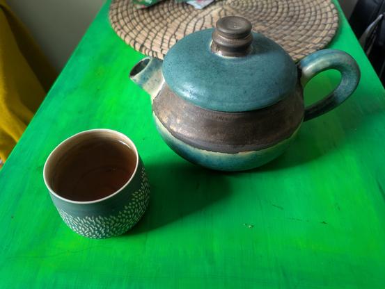 Un tasse de thé et un théière, les deux sont verte.

Le tasse avec de petites divots en Blanc.
Le théière est courte et ronde avec un court gros bec. Il y a un gros rayon  dessous le couverture en gris et bronze.