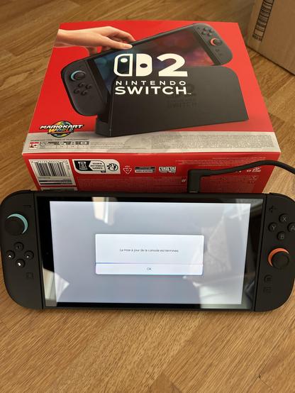 La Nintendo Switch 2 posé sur sa béquille avec ses deux joycons branchés. 
L’écran indique que la mise à jour a été effectuée.